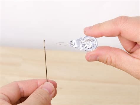 How do you thread an embroidery needle with a needle threader?
